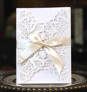Detailed laser-cut white invitation card featuring a champagne satin bow on elegant tray