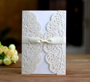 Detailed laser-cut ivory floral wedding invitation with silk ribbon on wooden table