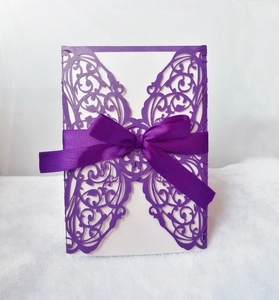 Macro detail of purple laser-cut wedding invitation with intricate vine patterns and ribbon