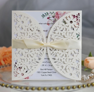 Detail of laser-cut floral wedding invitation with beige ribbon and floral inner card