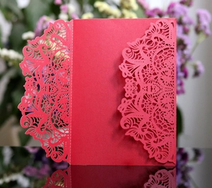 Close-up of red laser-cut wedding invitation with intricate floral lace patterns