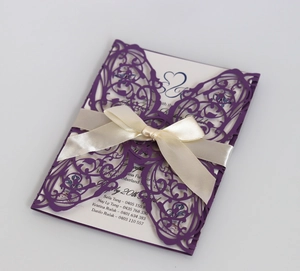 Macro view of purple laser-cut wedding invitation with elegant satin bow and insert
