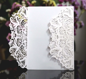 Close-up of laser-cut wedding invitation featuring intricate white lace floral patterns
