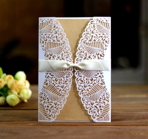 Close-up of laser-cut floral wedding invitation with kraft paper and white silk ribbon