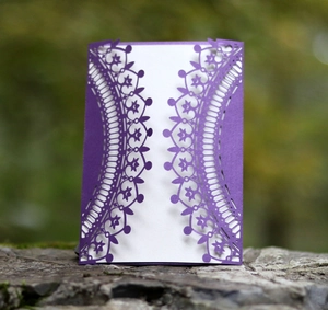 Macro shot of laser-cut purple invitation sleeve with intricate vintage scrollwork pattern