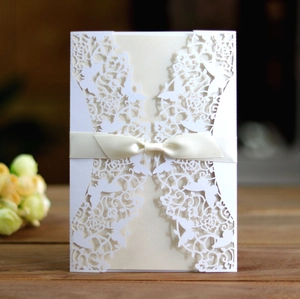 Detailed laser-cut wedding invitation with elegant butterfly lace and satin bow on wood
