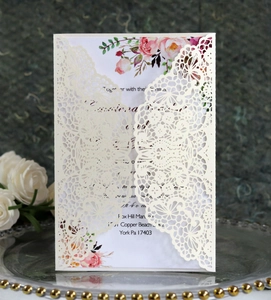 Detail of laser-cut lace wedding invitation with floral insert on decorative tray