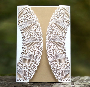 Detail of laser-cut leaf pattern on white wedding invitation with kraft paper insert