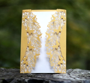 Macro shot of gold laser-cut invitation card with floral butterfly lace on rock base