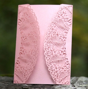 Close-up of pink laser-cut invitation card with floral patterns on stone surface