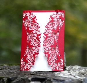 Detailed laser-cut wedding invitation with intricate butterfly and floral patterns on red cardstock