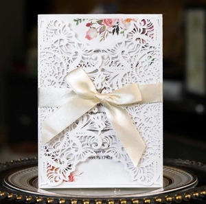 Detail of laser-cut wedding invitation with floral insert and cream satin ribbon bow