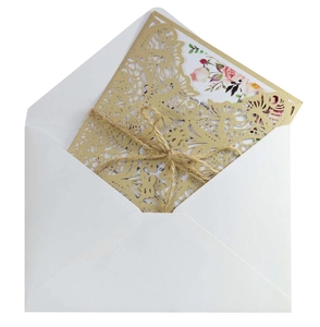 Detail of laser-cut gold wedding invitation with floral insert and rustic twine bow