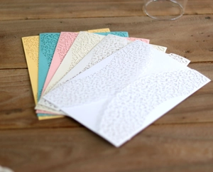Detail showing five laser-cut lace wedding invitations on dark wooden desk background