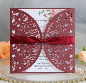Detail of burgundy laser-cut floral wedding invitation with silk bow and pink rose insert