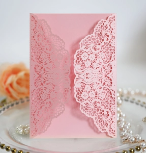 Detailed laser-cut lace pattern on pink wedding invitation with romantic floral background