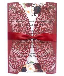Detail of laser-cut wedding invitation with burgundy floral lace and a red silk ribbon bow