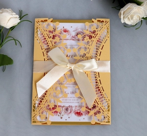 Detail of red laser-cut wedding invitation with gold crown lace and satin bow ribbon