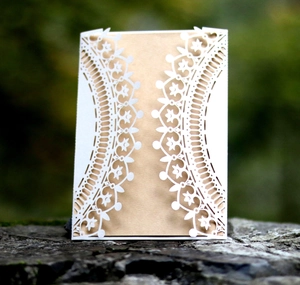 Detailed laser-cut floral lace invitation cover with brown kraft inner card on stone base