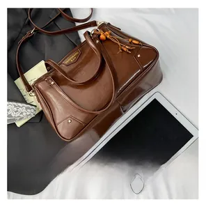 Detail of vintage brown leather tote bag showing wooden bead tassel and metal brand logo