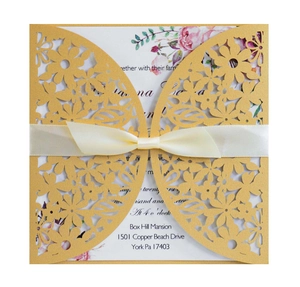 Detail of laser-cut gold wedding invitation with floral patterns and a cream silk ribbon