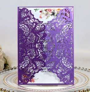 Detail of laser-cut purple wedding invitation with floral insert on a ceramic plate