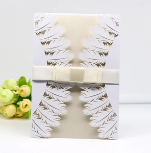 Detail of laser-cut feather hollow wedding invitation with champagne gold card and bow