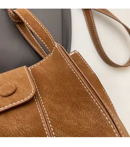 Gros plan détaillé du sac seau en cuir marron avec grain de litchi et coutures blanches
