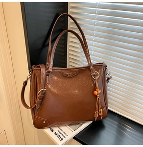 Detailed close-up of a vintage brown tote bag with metal logo and orange tassel charm