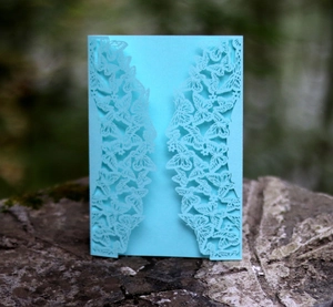 Detail of light blue laser-cut wedding invitation featuring butterfly and floral patterns