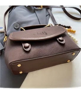 Detail of brown suede crossbody bag with gold hardware and side bead pendant on grey blazer