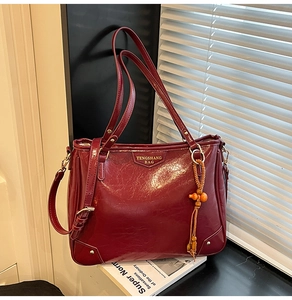 Detail of burgundy vintage tote bag with gold logo and wooden bead tassel accessory