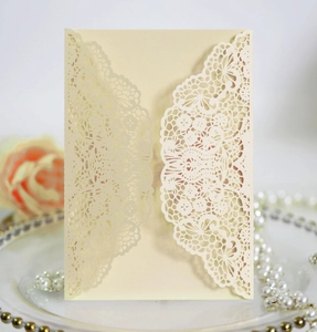 Detail of laser-cut lace wedding invitation cover on a tray with pearls and rose