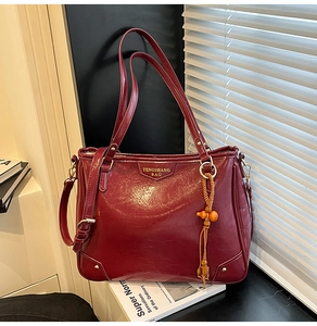 Detail of burgundy glossy PU leather tote bag with gold logo and woven wood bead charm