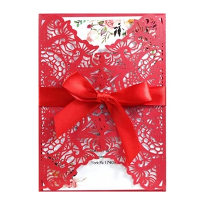 Macro view of laser-cut wedding invitation featuring intricate floral patterns and red ribbon