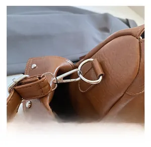 Close-up of brown leather bag with silver metal hook and decorative rivet details