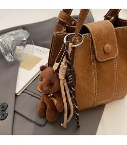 Détail du sac seau en similicuir marron avec coutures blanches et accessoire ours