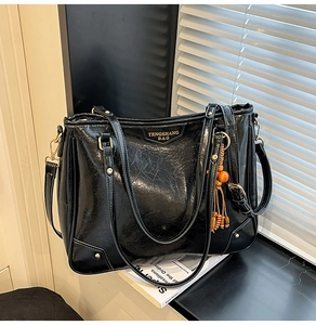 Detail of black crinkled patent leather tote bag with gold logo and tassel charm