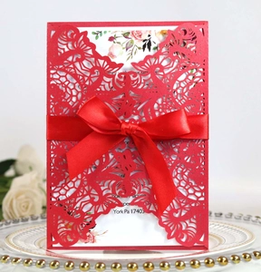 Close-up of laser-cut red wedding invitation with silk bow on decorative plate