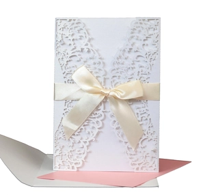 Detail of laser-cut lace wedding invitation with cream satin bow and pink insert card