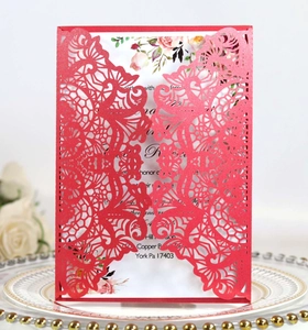 Macro detail of laser-cut red wedding invitation with floral white insert on a plate