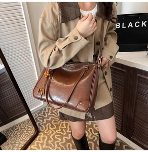 Detail of vintage brown glossy leather tote bag with wooden bead tassel and metal logo
