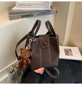 Brown vintage bucket bag with white contrast stitching and a cute bear bag charm accessory