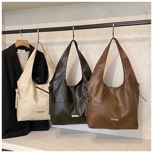 Three retro faux leather tote bags in cream, olive, and brown hanging on a metal display
