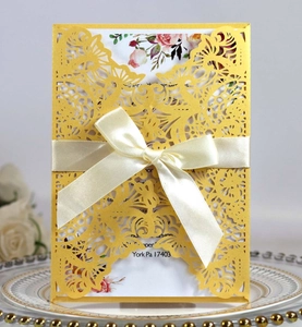 Detail of laser-cut yellow wedding invitation with floral insert and beige satin ribbon