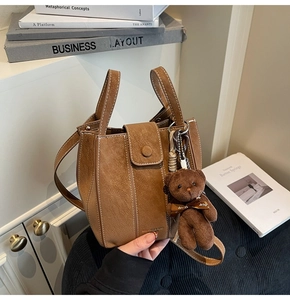 Detail of brown suede bucket bag with contrast stitching and plush bear charm