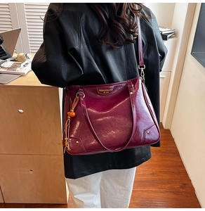 Close-up of wine red wrinkled leather tote bag with gold logo and wooden bead tassel