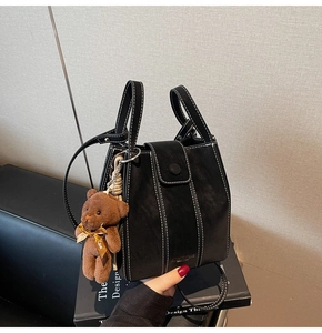 Detail of black vintage leather bucket bag with contrast stitching and bear charm