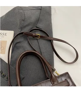 Detail of dark brown faux leather shoulder bag with vintage crocodile texture and long strap