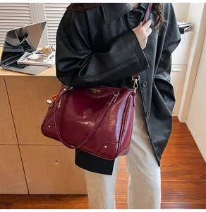 Detail of burgundy glossy leather tote bag with gold hardware and beaded pendant